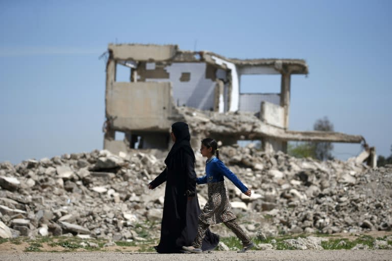 An Iraqi woman and a girl walk past destroyed buildings in the western part of Mosul on April 5, 2017, as Iraqi forces advance in their offensive to retake the city from the Islamic State group