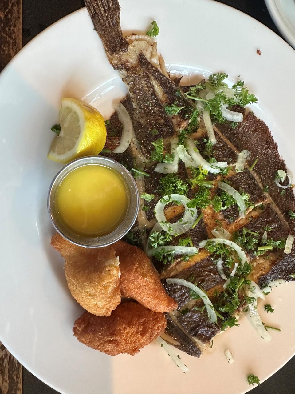 Broiled flounder topped with parsley and onion and served with butter and hush puppies at Angelo's Seafood Restaurant, March 16, 2024.