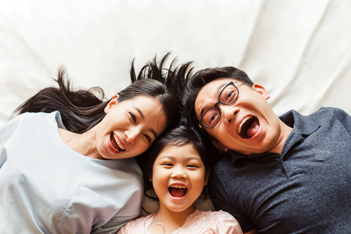 A family of three laugh as they lay down on a white sheet. 