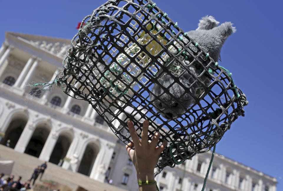 A girl holds up a fishing trap with a toy baby seal, in front of the Portuguese parliament in Lisbon as thousands of Portuguese high school students stage a protest while taking part in a global school strike for climate change Friday, March 15, 2019. Students worldwide are skipping class Friday to take to the streets to protest their governments' failure to take sufficient action against global warming. (AP Photo/Armando Franca)