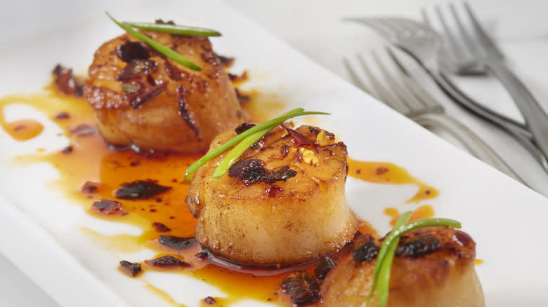 three scallops on a plate with chili oil