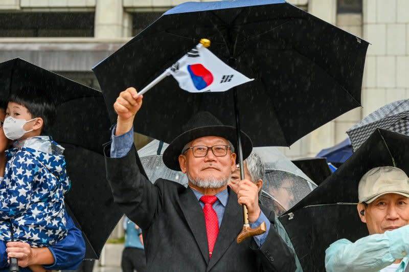 A spectator waves a South Korean flag in the rain during a military parade in Seoul Tuesday. Photo by Thomas Maresca/UPI