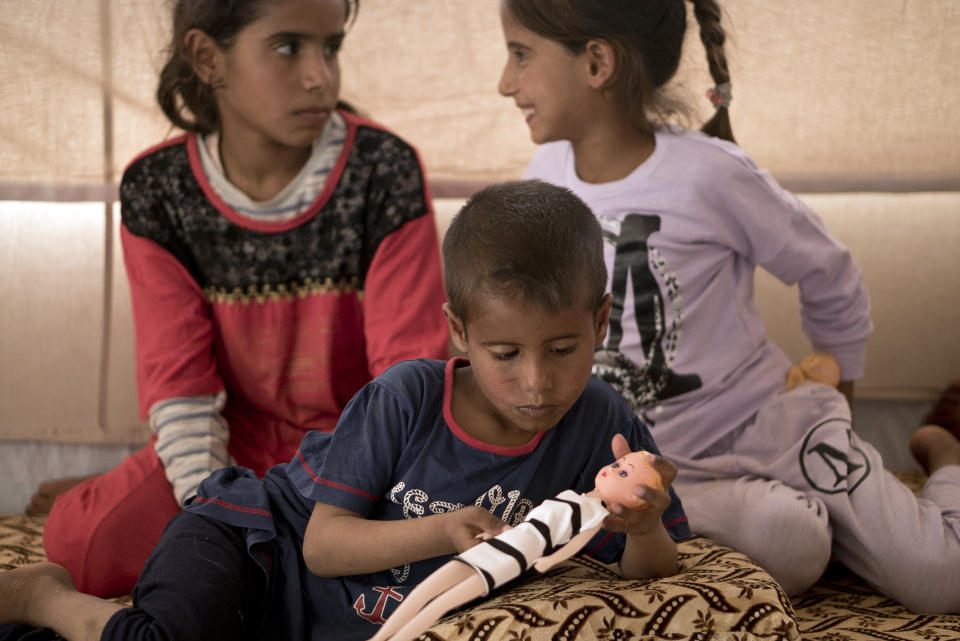 In this April 15, 2018 photo, Dawoud Suleiman plays with a doll as his sisters Dawlat, left, and Omaima, sit with him in their tent at Dakuk Camp, near Kirkuk, Iraq. Traumatized by a series of tragedies suffered during three years of fighting in Iraq, the children live under an additional burden: Their father and other family members belonged to the Islamic State group. (AP Photo/Maya Alleruzzo)