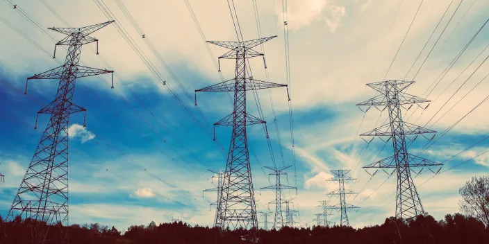 Layers of high tension electrical pylons and power lines against blue sky with clouds