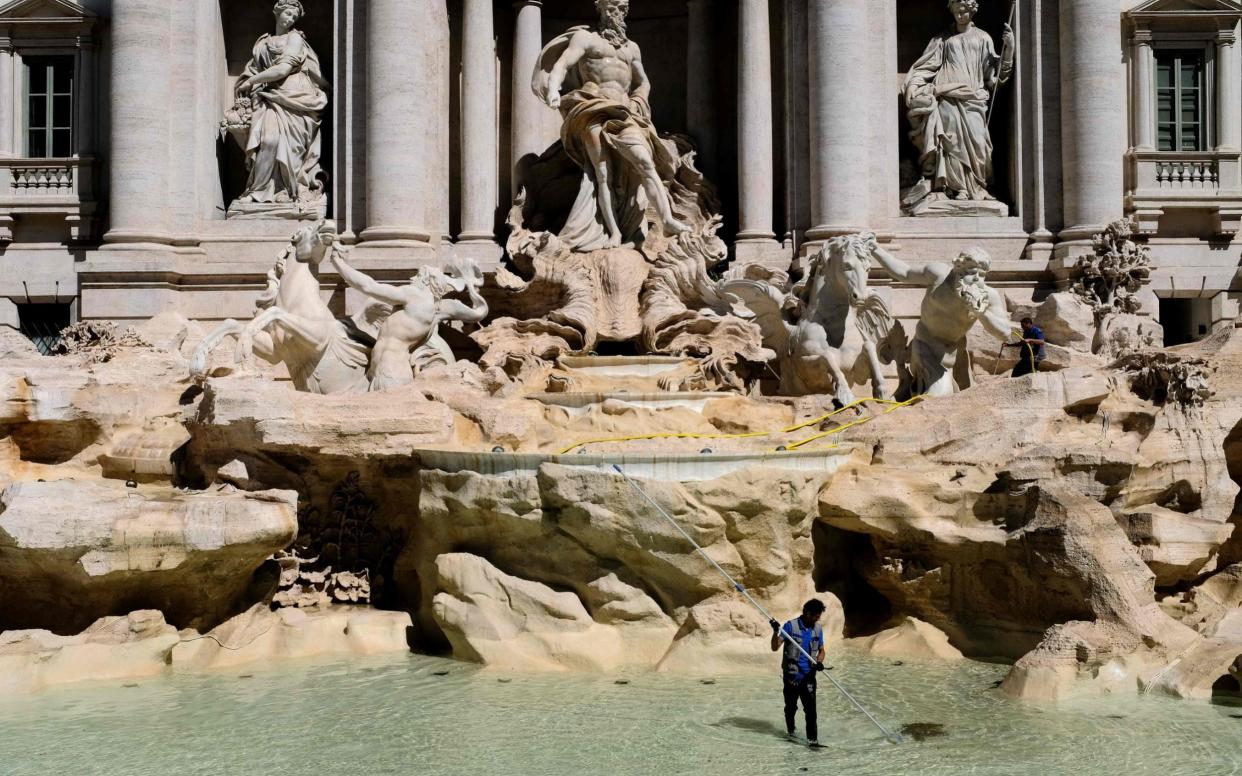 A worker collecting coins in the Trevi Fountain in Rome, as part of a regular monthly cleaning routine.  - AFP