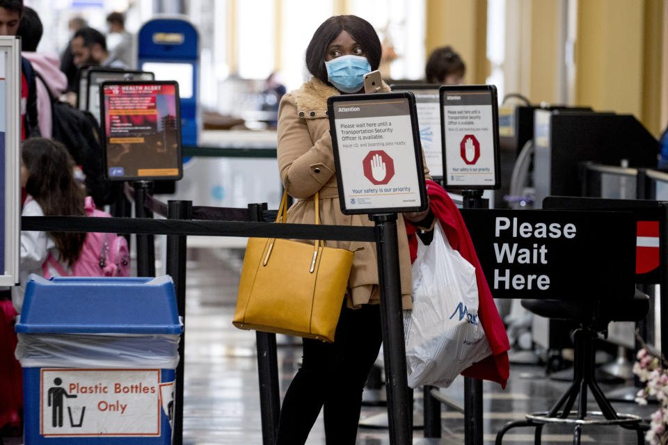 A woman wearing a mask walks goes through security at Ronald Reagan Washington National Airport, Monday, March 16, 2020, in Arlington, Va. (AP Photo/Andrew Harnik)