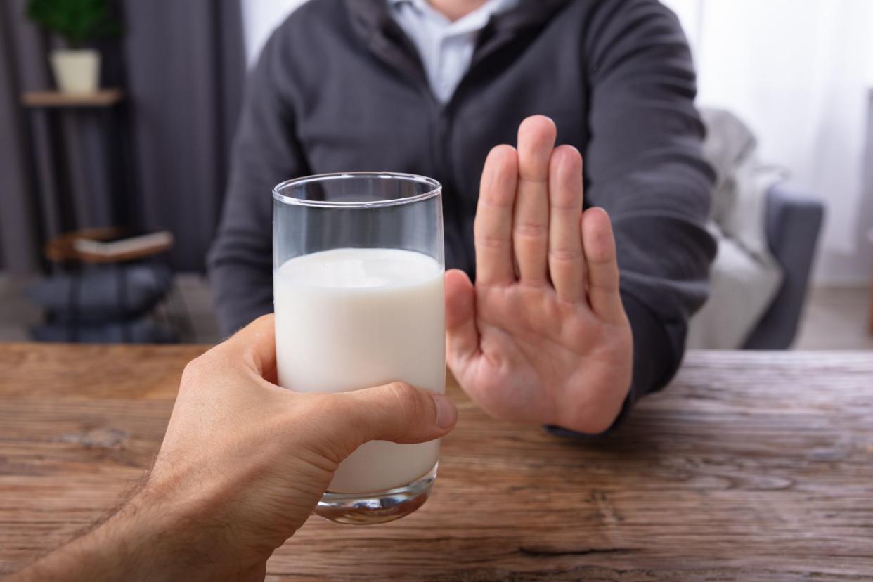 Close-up Of A Man Refusing Glass Of Milk Offered By Person Over Wooden Desk