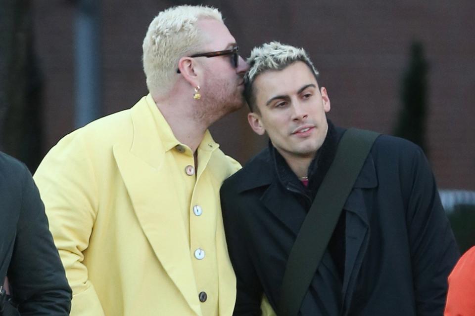 Singer Sam Smith sports a yellow jacket, rolled-up jeans and Bottega Veneta lug boots as they kiss a male friend while locking arms in Soho in New York City.