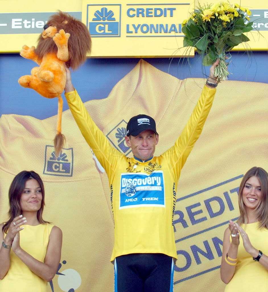 Armstrong with his arms raised holding flowers and a stuffed animal