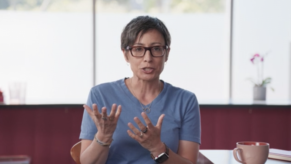 Feinberg talking and sitting in a chair with a coffee mug next to her