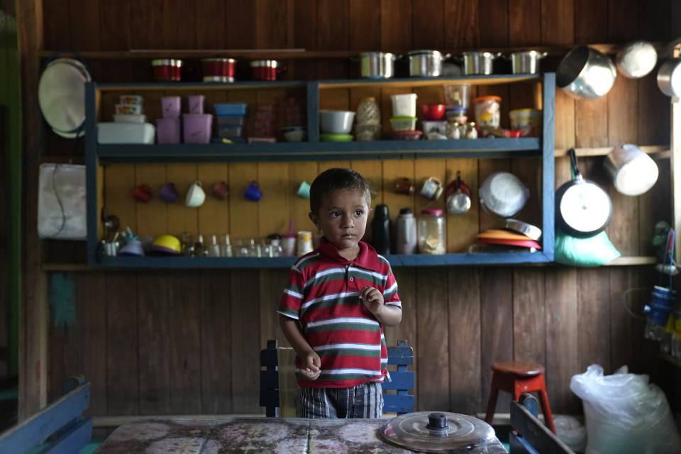 A boy stands at a table at a home in Lago Serrado community, near Carauari, Brazil, Thursday, Sept. 1, 2022. A Brazilian non-profit has created a new model for land ownership that welcomes both local people and scientists to collaborate in preserving the Amazon. (AP Photo/Jorge Saenz)