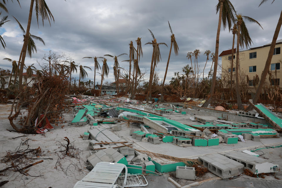 A scene of devastation, with a jumble of cinderblocks and denuded palm trees.