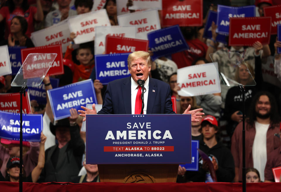 Former U.S. President Donald Trump bellowing at a podium, with an excited crowd behind him waving placards reading: Save America.