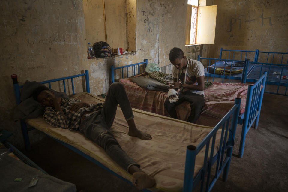 Abrahaley Minasbo a 22-year-old trained dancer, center, Tigrayan survivor from Mai-Kadra, Ethiopia, sits on a bed inside a shelter, in Hamdeyat Transition Center near the Sudan-Ethiopia border, eastern Sudan, Tuesday, Dec. 15, 2020. Minasbo said Amhara militia members dragged him from his home in Mai-Kadra on Nov. 9 and beat him in the street with a hammer, an axe, sticks and a machete, then left him for dead. Scars now slope across the right side of his face and neck. (AP Photo/Nariman El-Mofty)