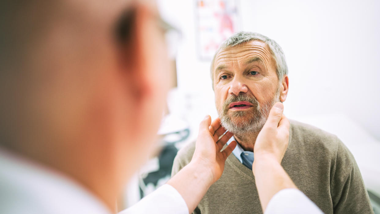 Over the shoulder view of a doctor touching a patient’s throat while doing a medical exam.