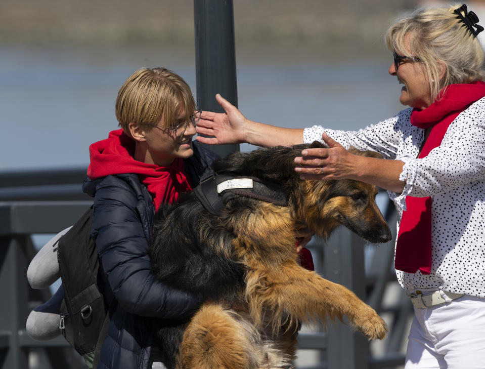 Tymon hugs his dog Bayca as his mother Anette Lange, right, runs to hug him, after Tymon disembarked from a schooner carrying 25 Dutch teens who sailed home from the Caribbean across the Atlantic when coronavirus lockdowns prevented them flying arrived at the port of Harlingen, northern Netherlands, Sunday, April 26, 2020. (AP Photo/Peter Dejong)