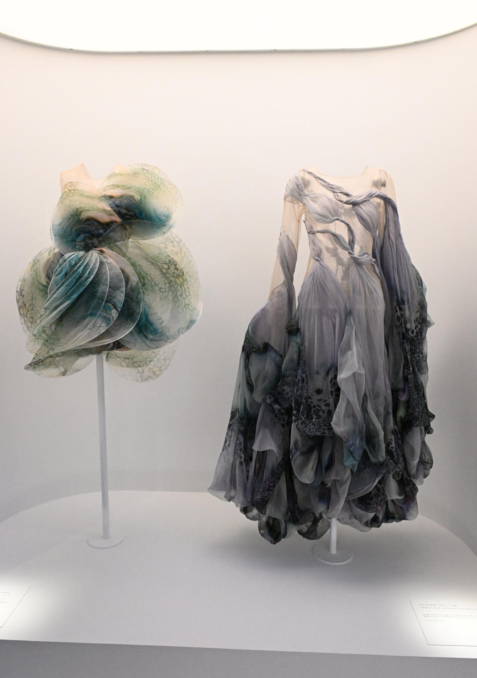 Two unique dresses on mannequins displayed in an exhibit, one with a voluminous, layered design