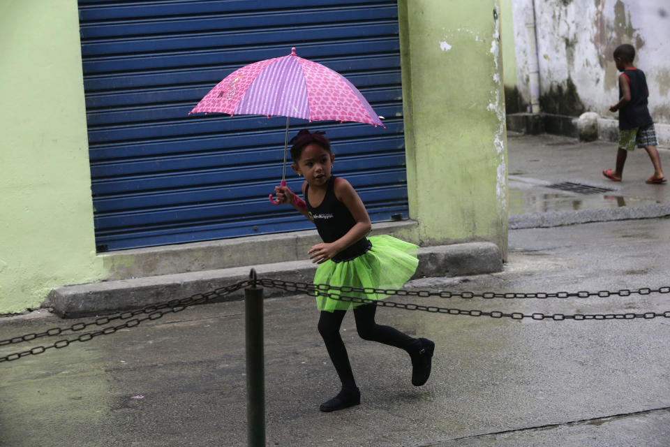 A young dancer from the Afro Reggae center covers herself from the rain after performing for members of London's Royal Opera House in the Vigario Geral slum in Rio de Janeiro, Brazil, Saturday, March 2, 2013. This past week Royal Ballet dancers shared their knowledge and advice with promising artists during an education symposium between the company and the cultural arts center Afro Reggae. (AP Photo/Silvia Izquierdo)