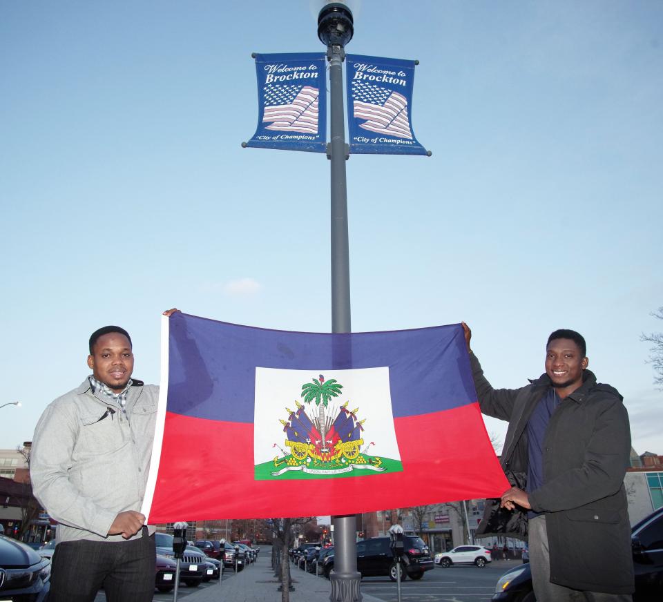 Brothers Therry Adamsley Gerard Volmar, 28, and Kercoff Sauphony Volmar, 26, proudly display the Haitian flag underneath a Welcome to Brockton sign in the downtown area on Monday, March 6, 2023.
