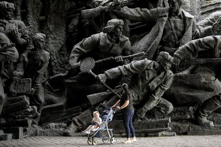 Una mujer empuja un cochecito de bebé mientras pasan junto a esculturas en bajorrelieve que representan escenas de guerra en el Museo Nacional de Historia de Ucrania durante la Segunda Guerra Mundial en Kiev, Ucrania, el lunes 8 de abril de 2024.