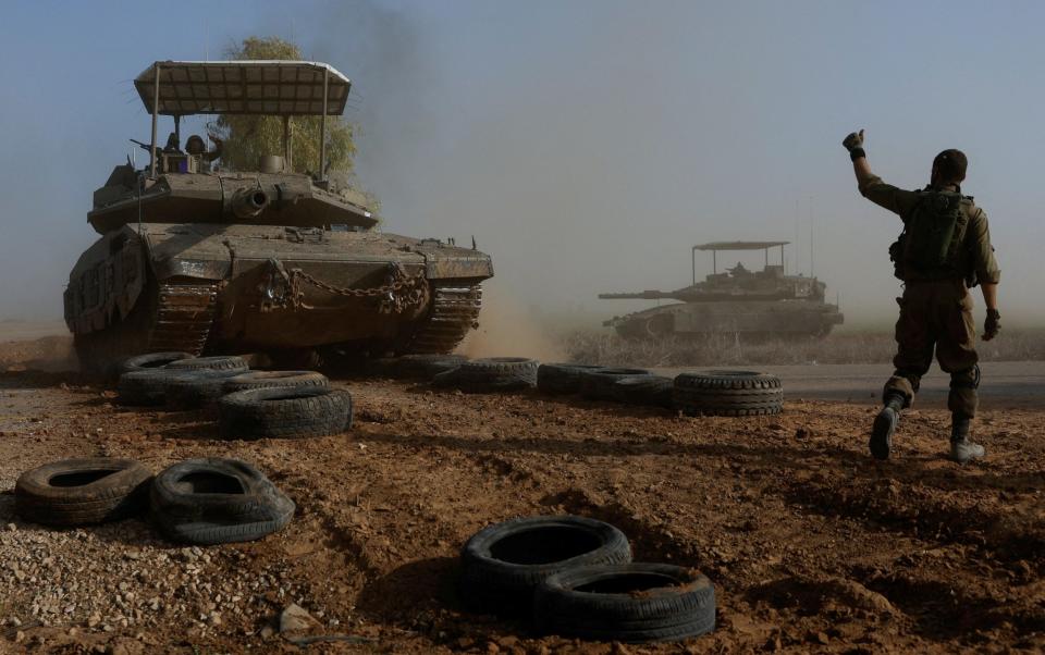 Israeli soldier gestures towards a tank crew member as it crosses a road near Israel's border with southern Gaza