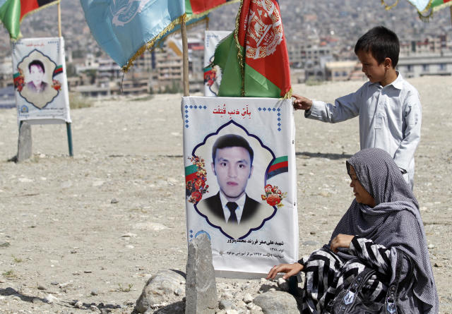 An Afghan woman site near to the grave of her son, adorned with his picture, on the outskirts of Kabul, Afghanistan, Monday, Sept 14, 2020. Scores of friends and families of students who were killed in local conflicts are gathering in a cemetery to call for a permanent countrywide ceasefire from the parties to the intra-Afghan peace conference taking place in Doha, Qatar. (AP Photo/Rahmat Gul)
