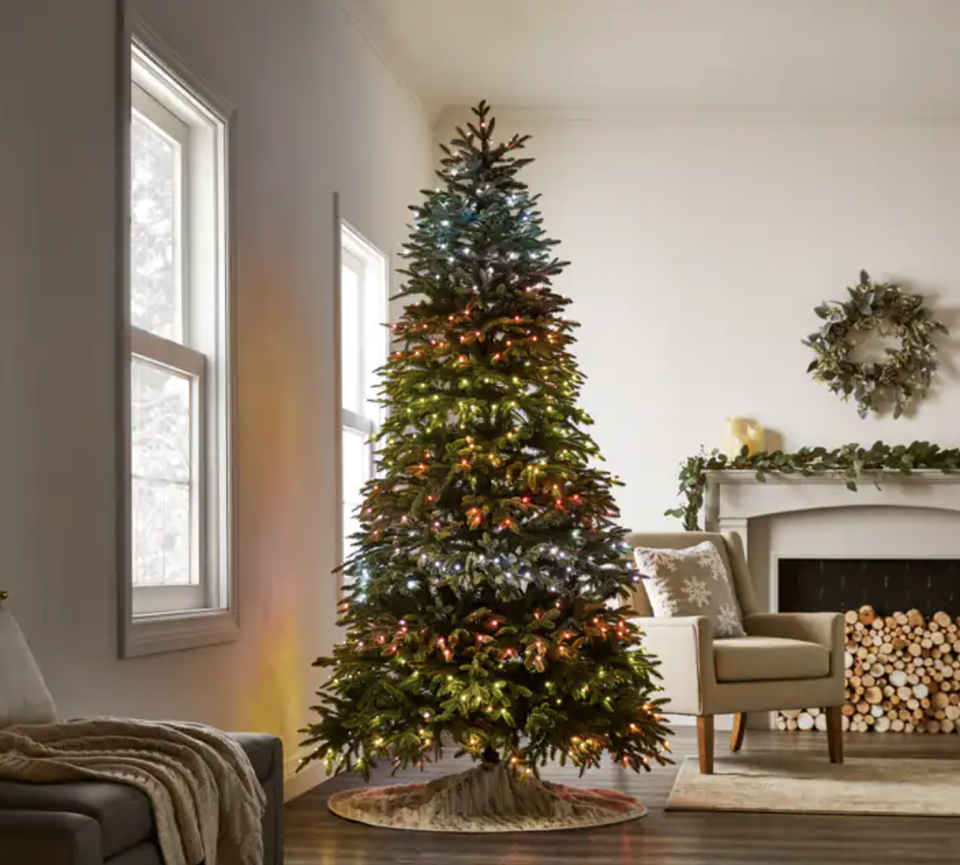 NOMA Advanced Aurora Music & Light Show Árvore de Natal na sala de estar junto à lareira (Foto via Amazon)