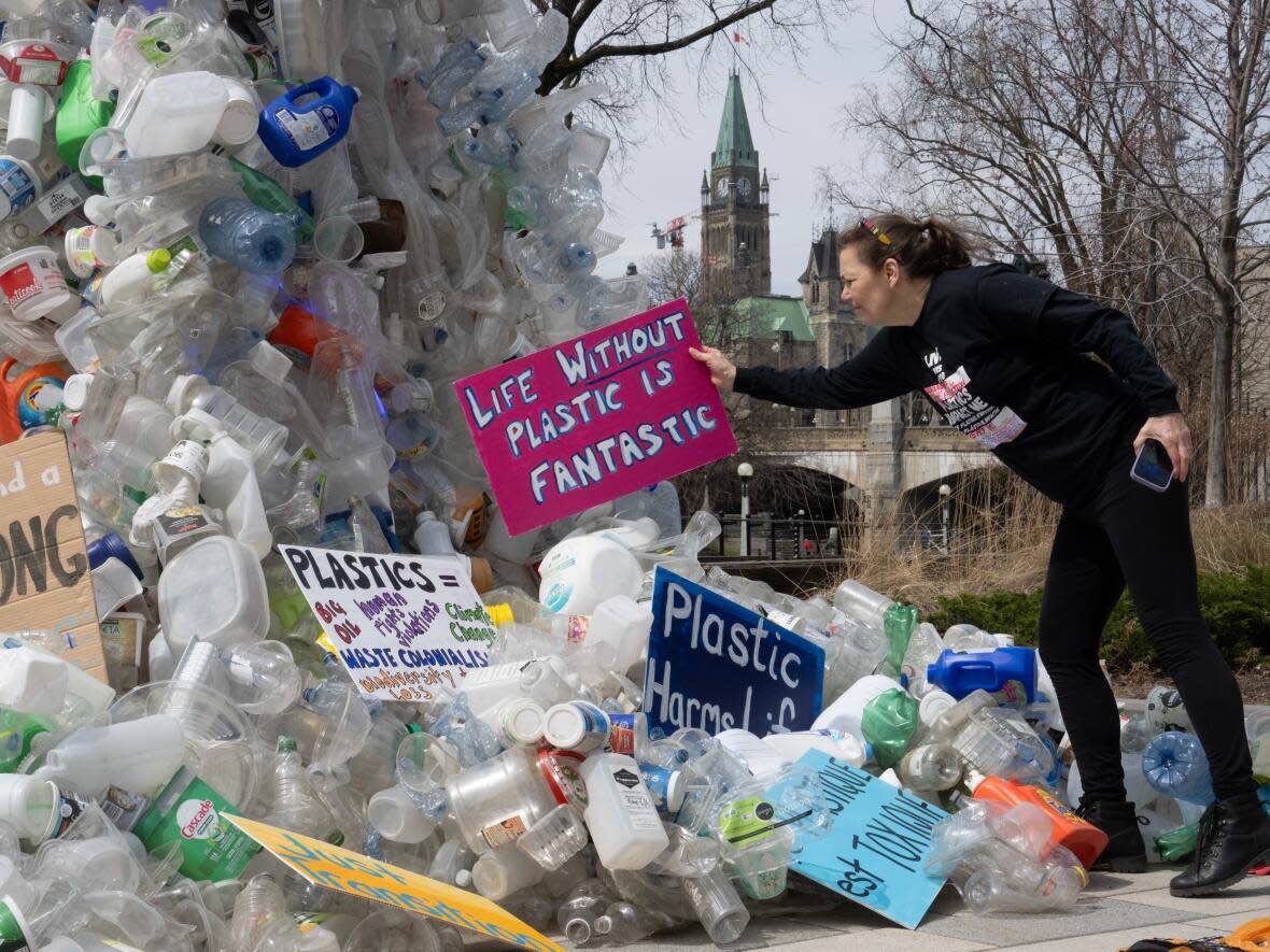Activist Dianne Peterson places a sign on a public art installation outside the conference on plastics in Ottawa, which wrapped up Tuesday in the early morning hours. (Adrian Wyld/The Canadian Press - image credit)