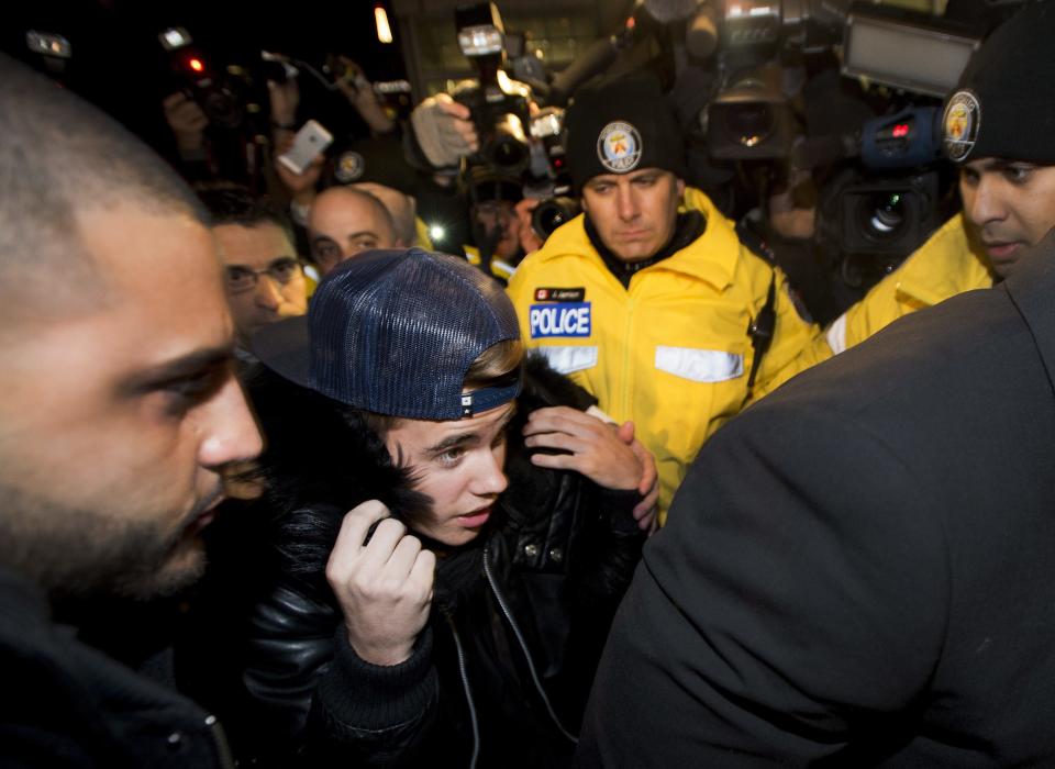 Canadian musician Justin Bieber is swarmed by media and police officers as he turns himself in to city police for an expected assault charge, in Toronto, on Wednesday, Jan. 29, 2014. A police official said the charge has to do with an alleged assault on a limo driver in December. (AP Photo/The Canadian Press, Nathan Denette)