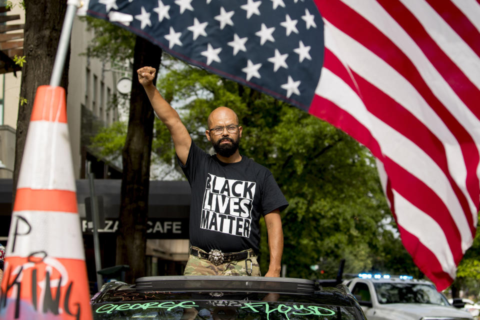 FILE - In this June 19, 2020, file photo, George Floyd's name is written on the windshield as John Coy wears a shirt that reads Black Lives Matter and stands through his sunroof with his fist in the air at 16th Street Northwest renamed Black Lives Matter Plaza near the White House in Washington. Thousands of Black activists from across the U.S. will hold the 2020 Black National Convention on Aug. 28, 2020, via livestream to produce a new political agenda that builds on the protests that followed George Floyd’s death. Organizers of the gathering shared their plans with The Associated Press on Wednesday, July 1, ahead of an official announcement. (AP Photo/Andrew Harnik)