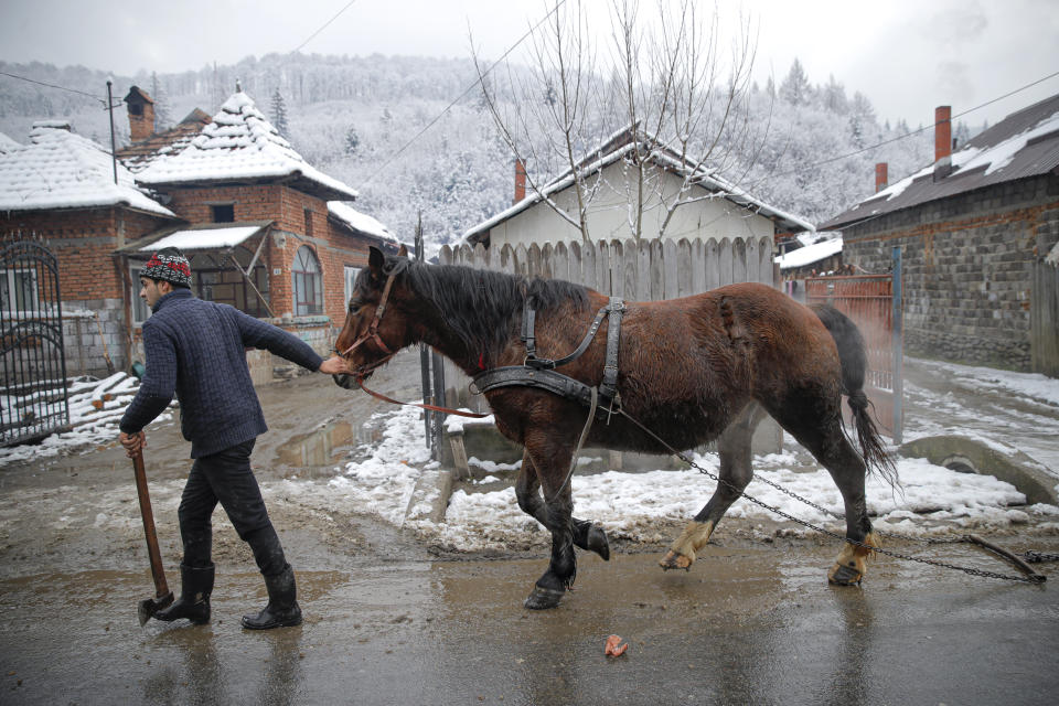 A man holds an axe while walking with a horse in Leresti, Romania, Saturday, Jan. 9, 2021. Valeriu Nicolae and his team visited villages at the foot of the Carpathian mountains, northwest of Bucharest, to deliver aid. The rights activist has earned praise for his tireless campaign to change for the better the lives of the Balkan country’s poorest and underprivileged residents, particularly the children. (AP Photo/Vadim Ghirda)