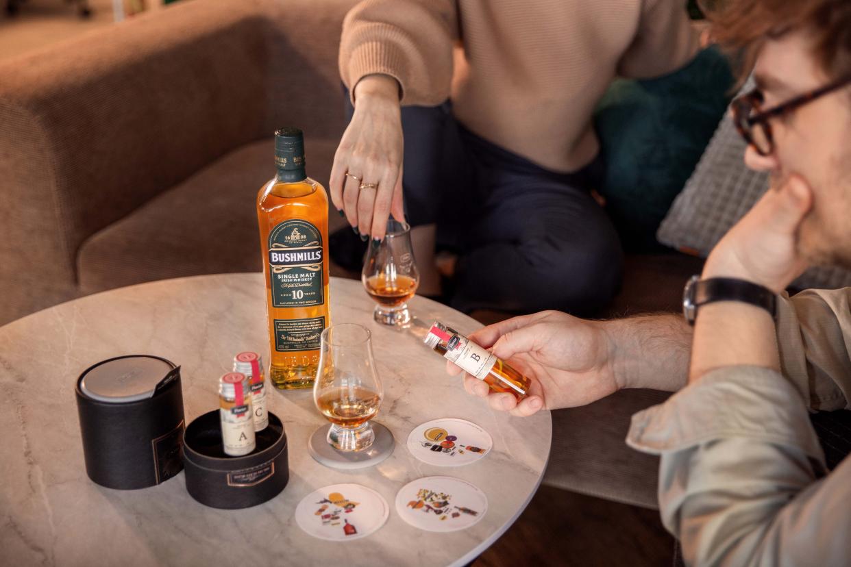 A couple at home sitting on an 'L'-shaped couch around a white marble coffee table with Flaviar drinking samples, soft lighting from top left