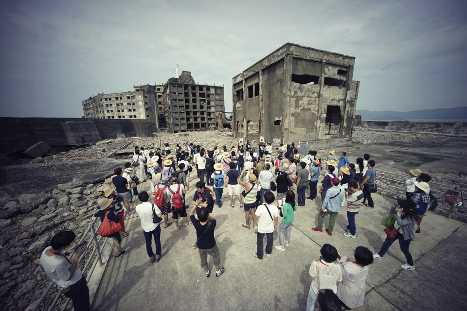 FILE - In this June 29, 2015, file photo, tourists visit a part of Hashima Island, commonly known as Gunkanjima, which means "Battleship Island," off Nagasaki, Nagasaki Prefecture, southern Japan. Gunkanjima was among the settings for a dark chapter in Japan’s history, when hundreds of thousands of people were brought from the Korean Peninsula and other Asian nations to work in logging, in mines, on farms and in factories as forced labor. (AP Photo/Eugene Hoshiko, File)