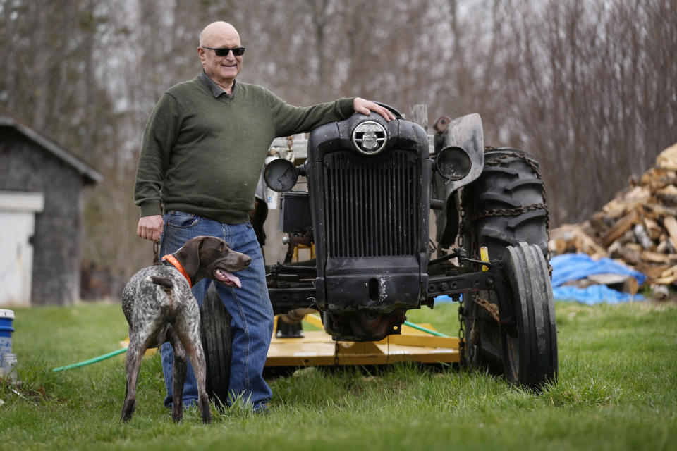 Charlie Robbins stands next to his tractor at his home, Wednesday, April 26, 2023, in Columbia Falls, Maine. Robbins, an ardent sportsman, is opposed to a plan to build an enormous flagpole and theme park on undeveloped land cherished by hunters and fishermen. He doesn't question the motives of the flagpole. “It’s just different than my vision,” he says. “I hunt and fish the area. I don’t like the crowds. It’s kind of selfish, but that’s the way I feel." (AP Photo/Robert F. Bukaty)