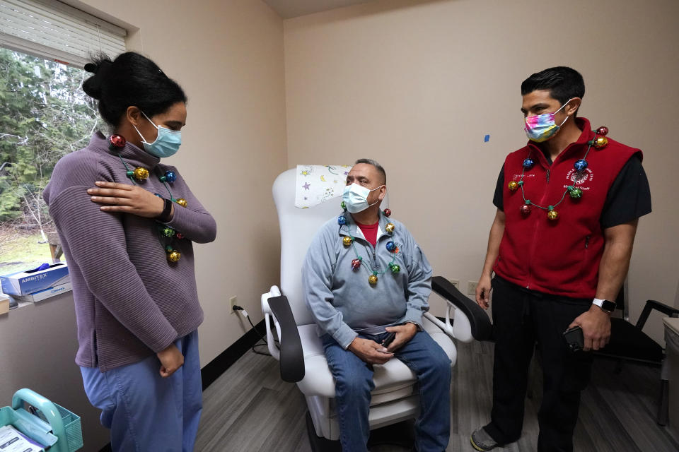 Dr. Dakotah Lane, right, looks on as Dr. Cristina Toledo-Cornell explains possible arm soreness to James Scott after Scott received the first COVID-19 vaccination given to a Lummi Nation tribal member Thursday, Dec. 17, 2020, on the Lummi Reservation, near Bellingham, Wash. The Native American tribe began rationing its first 300 doses of vaccine as it fights surging cases with a shelter-in-place order. (AP Photo/Elaine Thompson)