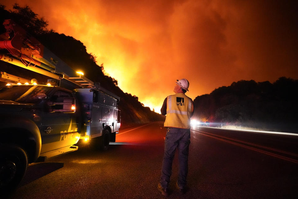 FILE - In this Tuesday, Sept. 8, 2020 file photo, A Pacific Gas and Electric worker looks up at the advancing Creek Fire along Highway 168 near Alder Springs, Calif. Pacific Gas & Electric will cut power to over 1 million people on Sunday to prevent the chance of sparking wildfires as extreme fire weather returns to the region, the utility announced Friday. Oct. 23, 2020. (AP Photo/Marcio Jose Sanchez, File)