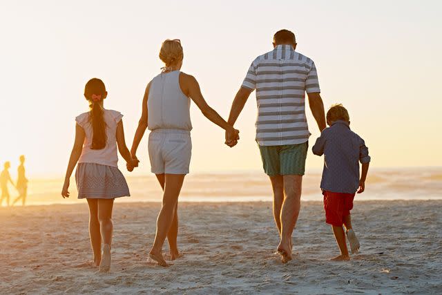 <p>Getty</p> Stock image ofparents and children holding hands while walking on beach.