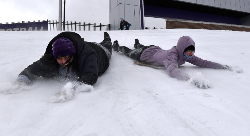 Gabriella Lopez (left) and Issy Birsinger slide belly-first down a snowy hill at Abilene Christian University in February 2022.