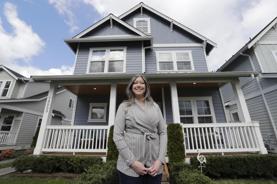 In this Wednesday, April 1, 2020 photo, Rebeka McBride stands in front of her home that is in the process of being sold in Monroe, Wash., outside of Seattle. She put her house on the market in early March and is in the process of closing on the sale. But with the U.S. economy now collapsing, the family is less confident about their move to a Minneapolis suburb, where McBride sees brighter job prospects in her field of medical device research.(AP Photo/Elaine Thompson)