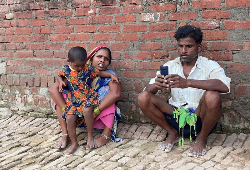 Asha Devi, a mother of five who is a labour worker, sits along with her husband and their daughter outside her one-room house in Dihwa