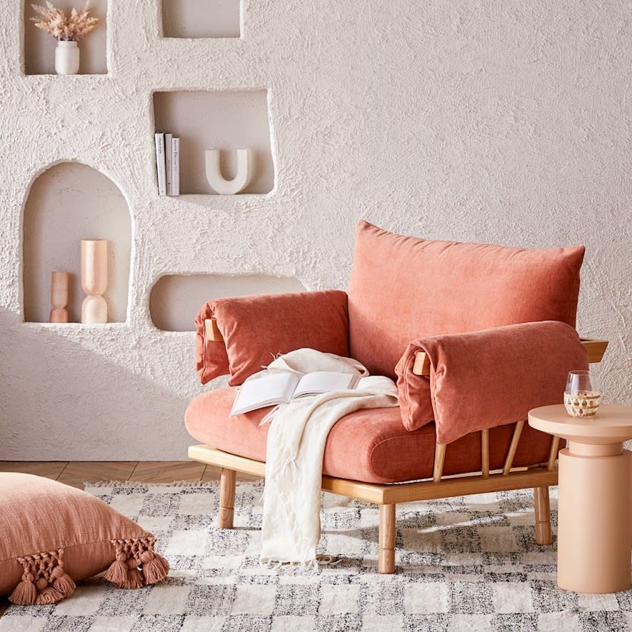 Neutral toned room featuring textured concrete wall with asymmetrical alcoves and bric-a-brac, luxuriously wide and comfortable salmon chair with off white throw and book