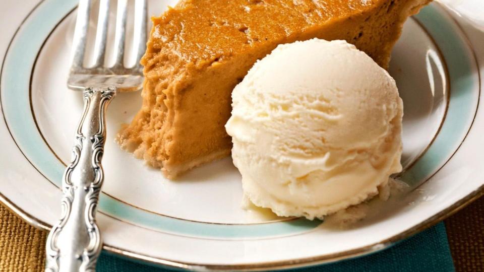 a slice of sweet potato pie on a white plate with a scoop of vanilla ice cream