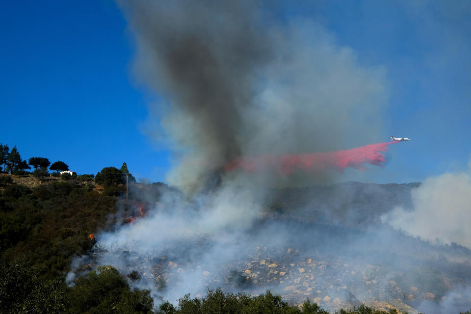 An air tanker drops retardant on a wildfire burning near a home Wednesday, Oct. 13, 2021, in Goleta, Calif. A wildfire raging through Southern California coastal mountains threatened ranches and rural homes and kept a major highway shut down Wednesday as the fire-scarred state faced a new round of dry winds that raise risk of infernos. (AP Photo/Ringo H.W. Chiu)