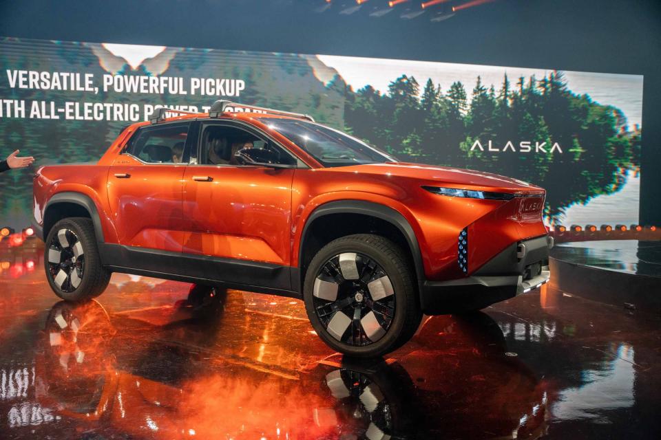 The orange Fisker Alaska electric pickup truck, on stage at an event.