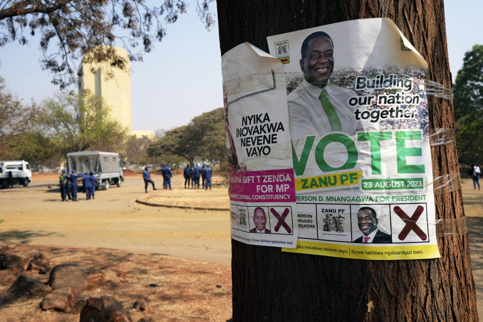 An election campaign poster with a portrait of Zimbabwean President Emmerson Mnangagwa is displayed on a tree while, in the background, armed riot police prepare to be deployed on the streets of Harare, Zimbabwe, Friday, Aug. 25, 2023. Hordes of police officers armed with batons, teargas canisters and some with guns were seen next to the result centre as Zimbabweans anxiously waited for the outcome of general elections after polls closed on Thursday and authorities tightened security around the results centre. (AP Photo/Tsvangirayi Mukwazhi)