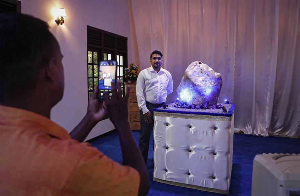 Sri Lankan gem enthusiasts take photos standing next to a 310 kilograms (683 pounds) heavy natural corundum blue sapphire at a residence where it is kept in Horana, about 41 kilometers (25 miles) south of Colombo, Sri Lanka, Sunday, Dec. 12, 2021. A gem company in Sri Lanka has unveiled the massive gemstone that is certified as a rare and one of the biggest corundums found in the country and plans to offer it to museums and gem collectors. (AP Photo/Eranga Jayawardena)