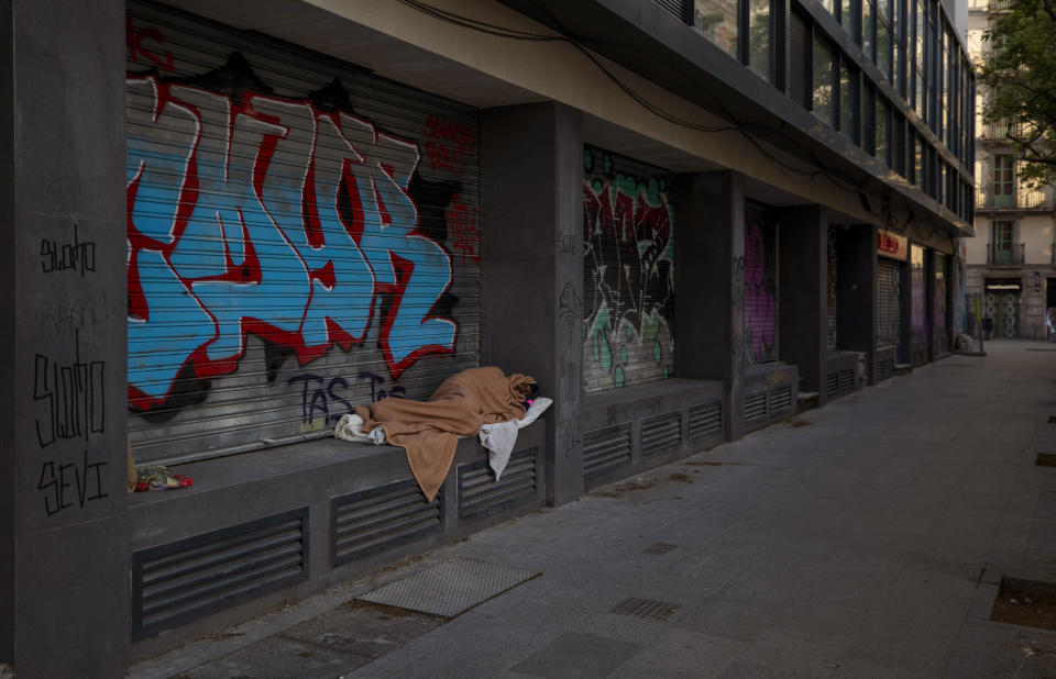 In this Friday, March 20, 2020 photo, Nasir, 37, from Pakistan, sleeps in an empty street in Barcelona, Spain. Authorities are scrambling to get as many homeless people off the streets without cramming them into a shelter, where the spread of COVID-19 could be even greater. (AP Photo/Emilio Morenatti)