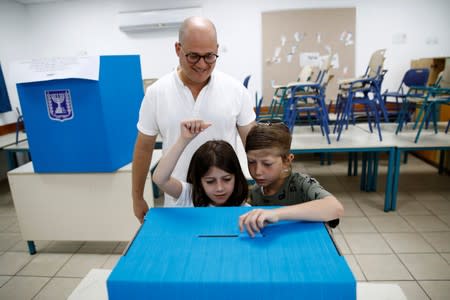 Children stand with their relative as they place his vote in a ballot box on Israel's parliamentary election, at a polling station in Tel Aviv, Israel