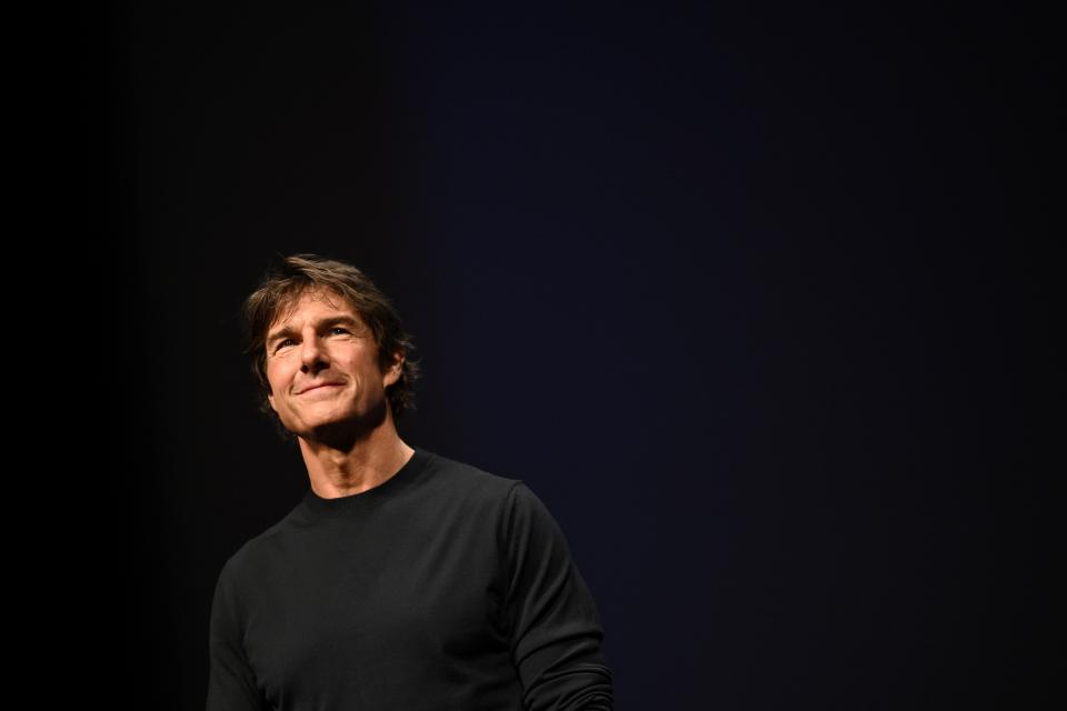 Tom Cruise wearing a black shirt and standing behind a black background