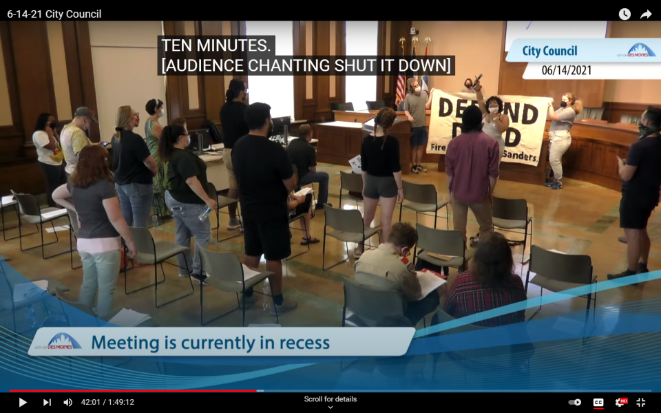 In this image captured from a City of Des Moines video, Paden Sheumaker can be seen leading protest chants in front of a "Defund DMPD" banner during the June 14 meeting of the City Council.